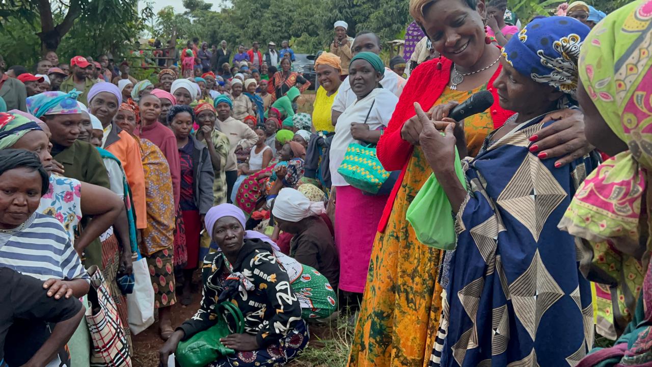 A woman speaking into a microphone at a rural community gathering of women farmers