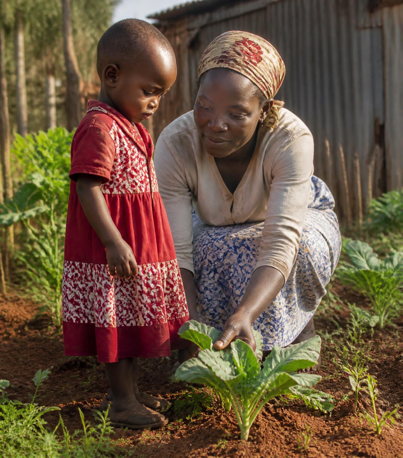 A Kenyan mother showing her young daughter a vegetable seedling in their kitchen garden